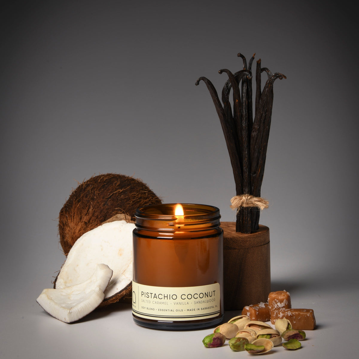 Amber candle jar with lit wick alongside coconut half and pistachio shells.