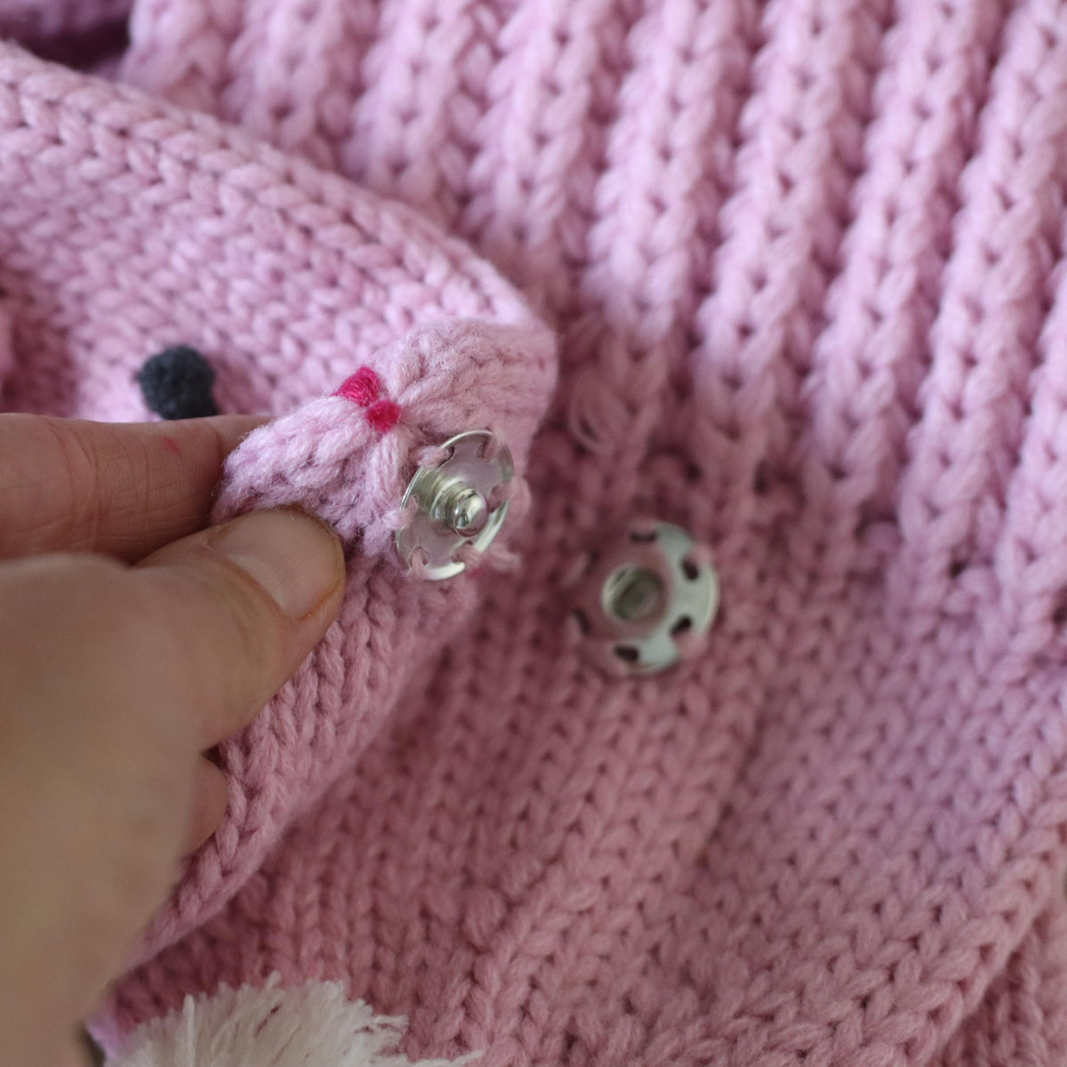 Pink knitted bunny scarf close-up showing its snap fastener and textured stitches