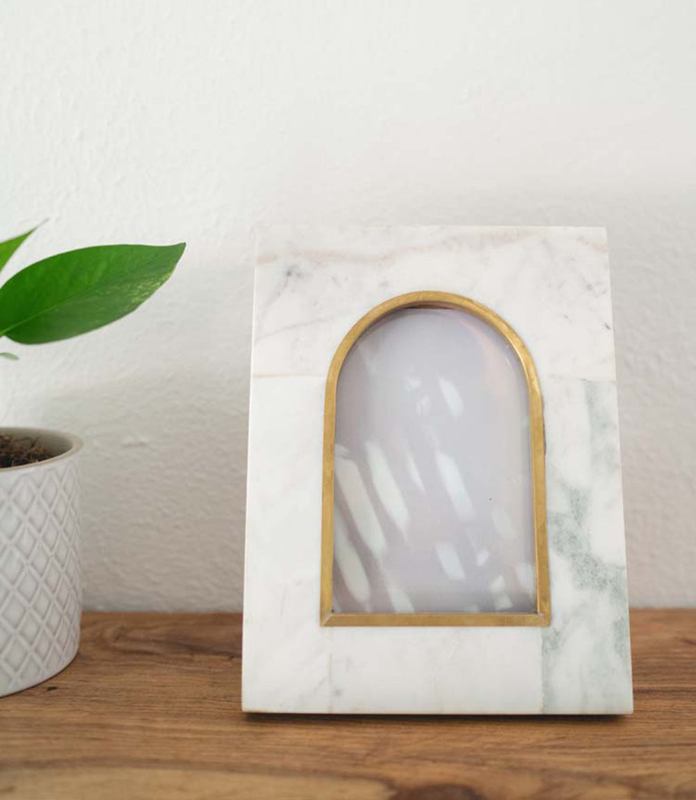 Arched white marble picture frame with brass gold trim, standing on a surface