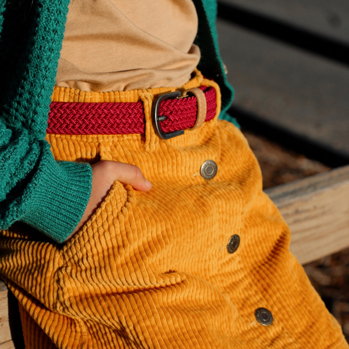 Girls' red braided stretch belt with tan leather trim and dark buckle, worn at the waist