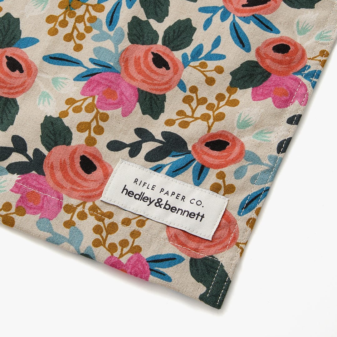 Floral crossback apron bottom hem with brand label and dark green side stitching.