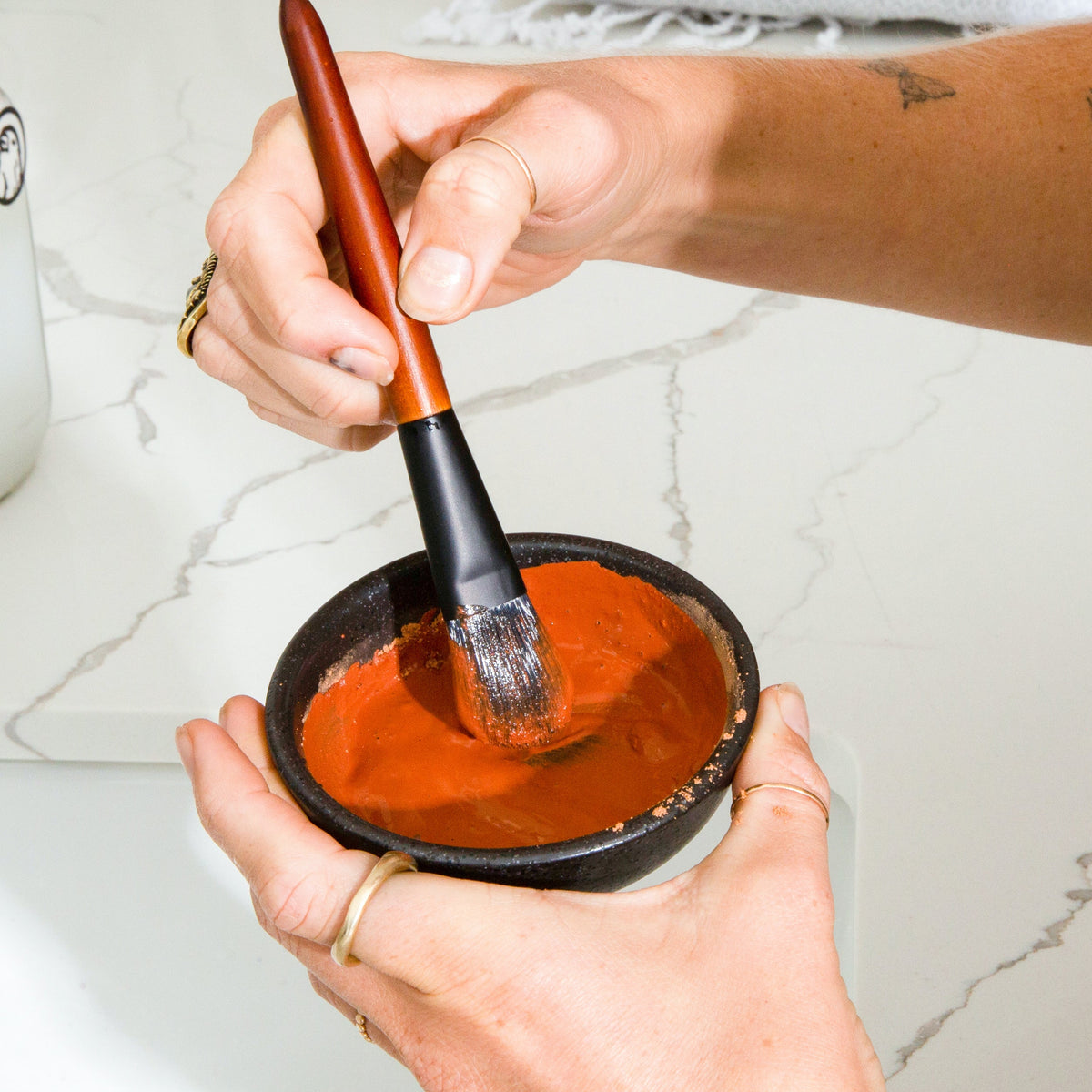 Orange clay face mask paste mixed in a bowl with a brush