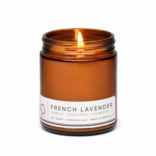 Amber soy candle in glass jar with lit wick, white label reading French Lavender