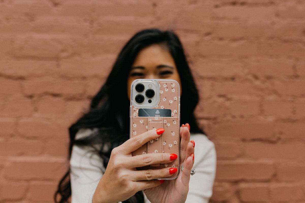 Brown floral phone case with white daisies, worn on a phone in hand