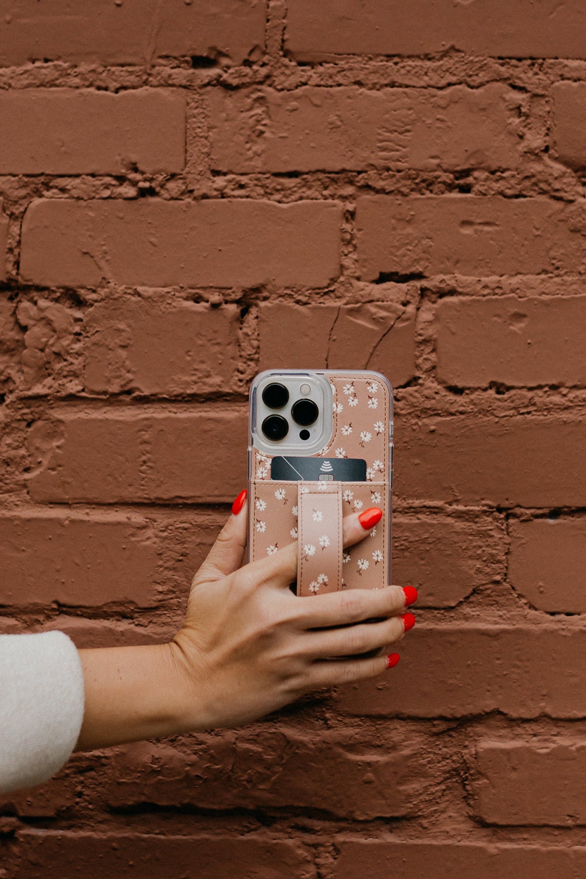 Brown floral phone case with white daisy pattern and card-holder pocket on phone