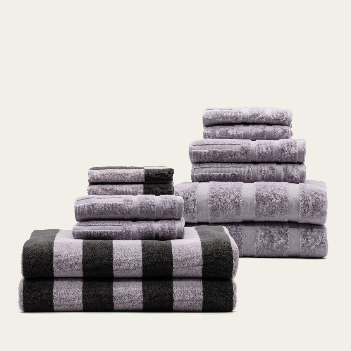 Assorted towels stacked in lilac and charcoal, including black-and-white striped towels