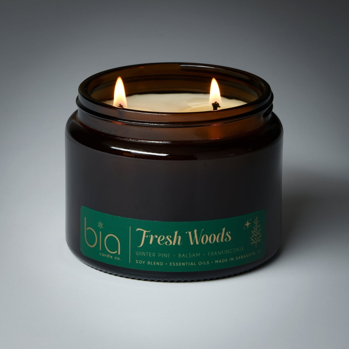 Amber glass soy candle jar with green Fresh Woods label and two lit wicks