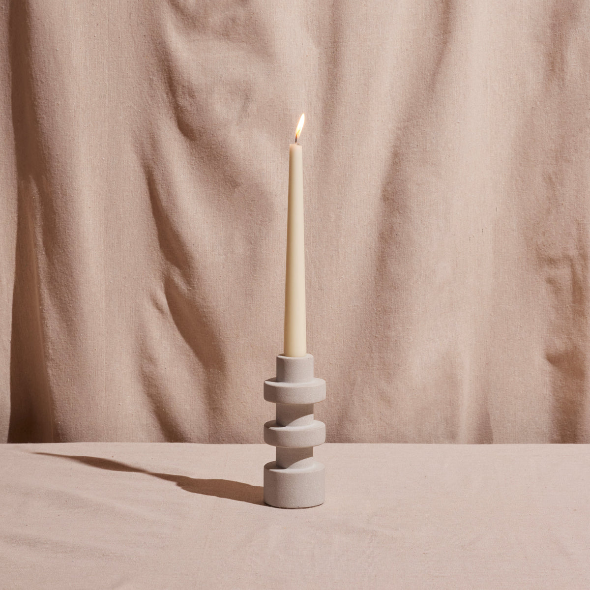 Tall candle holder with three stacked rings holding a white pillar candle.