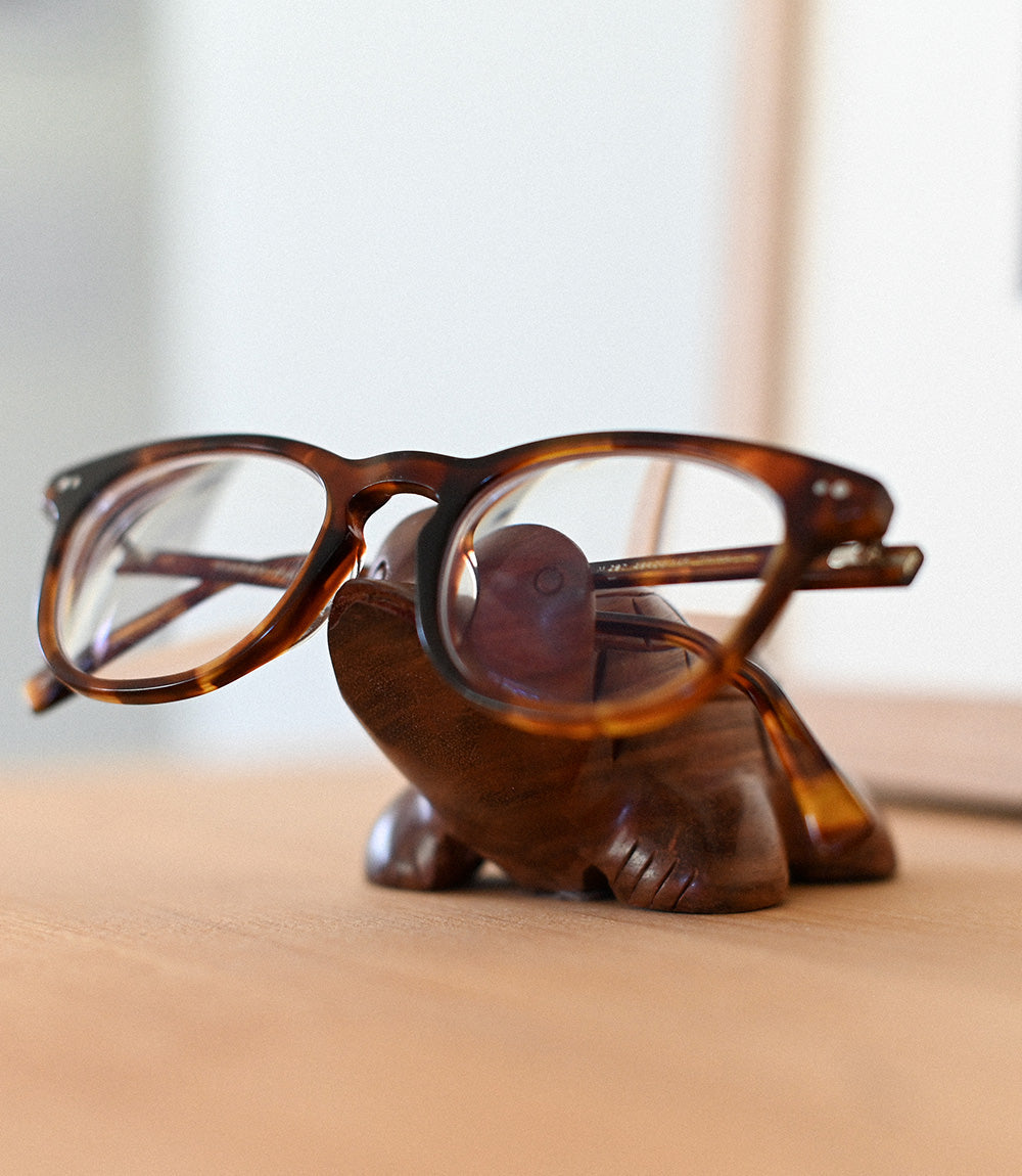 Tortoiseshell glasses sitting on a carved rosewood turtle eyeglasses stand.