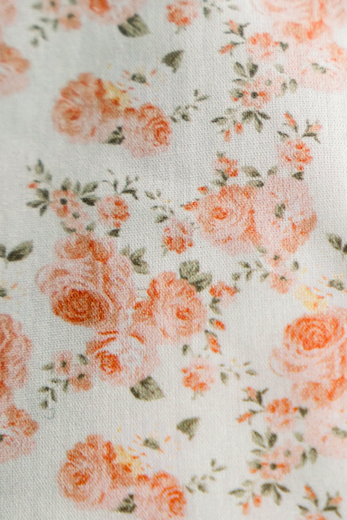 Close-up fabric texture with coral roses, orange flowers, and scattered green foliage