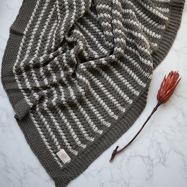 Dark gray-brown and white striped knit throw blanket with woven brand tag