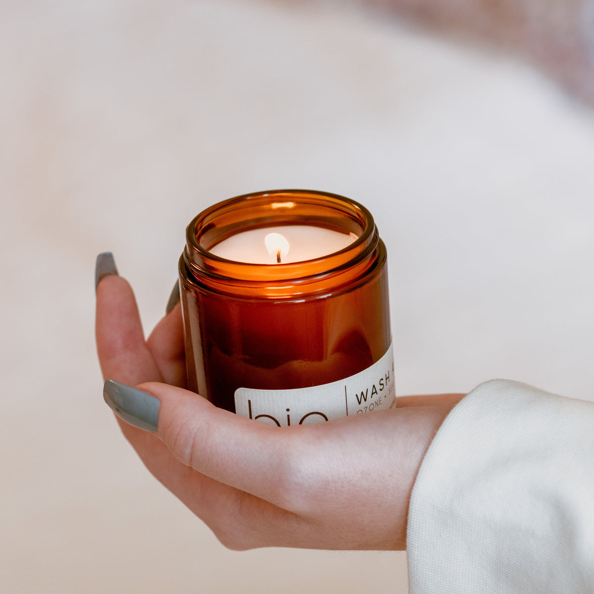 Lit amber glass candle jar with hands holding it, teal nail polish
