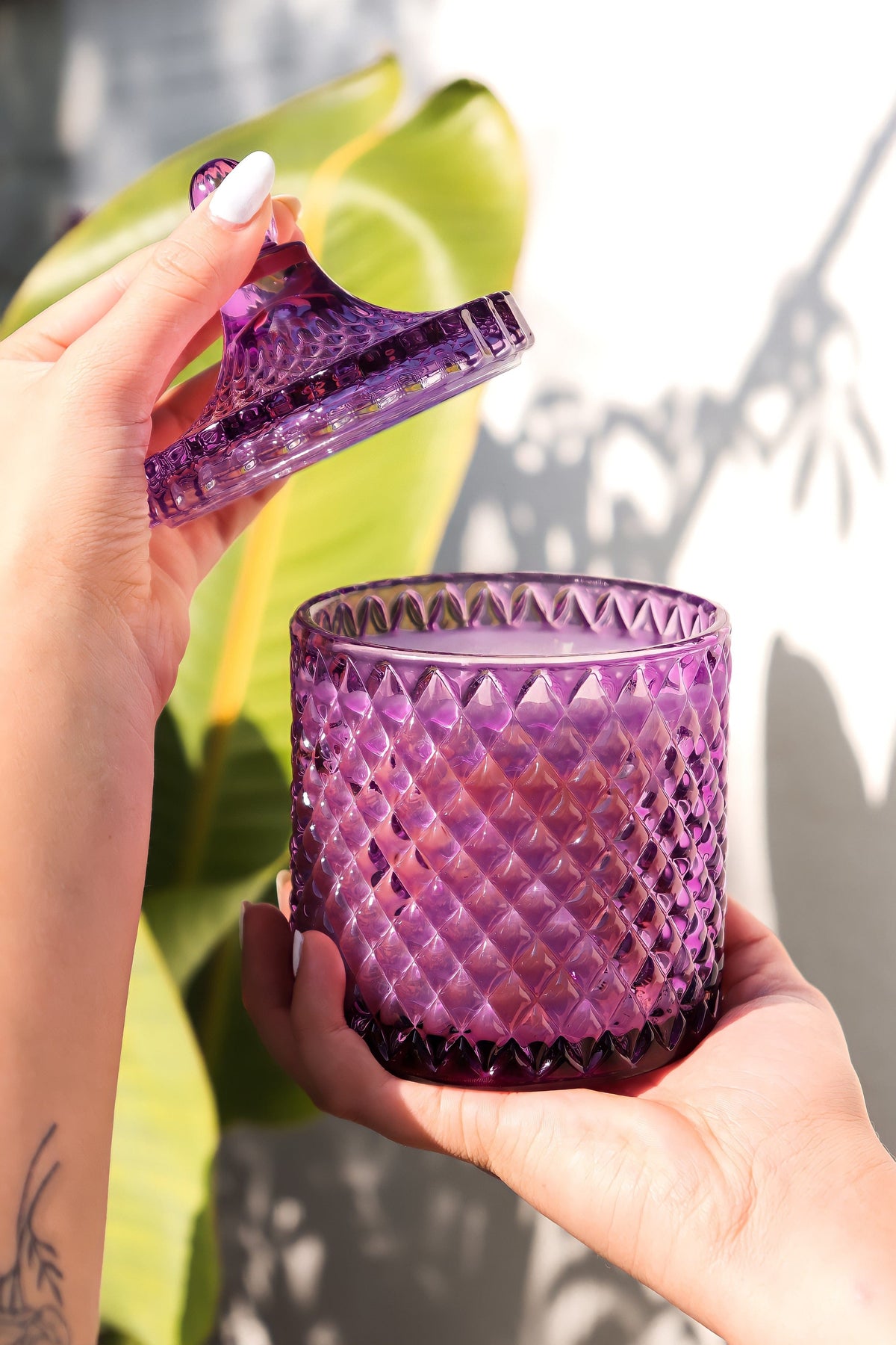 Purple faceted candle jar held in hands, clear lid topper visible