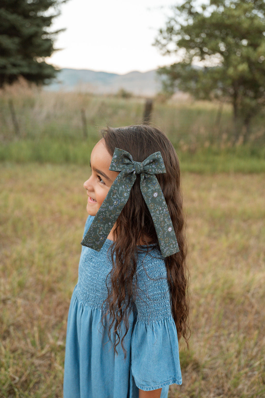 Girl wearing teal floral hair bow with long ribbon tails