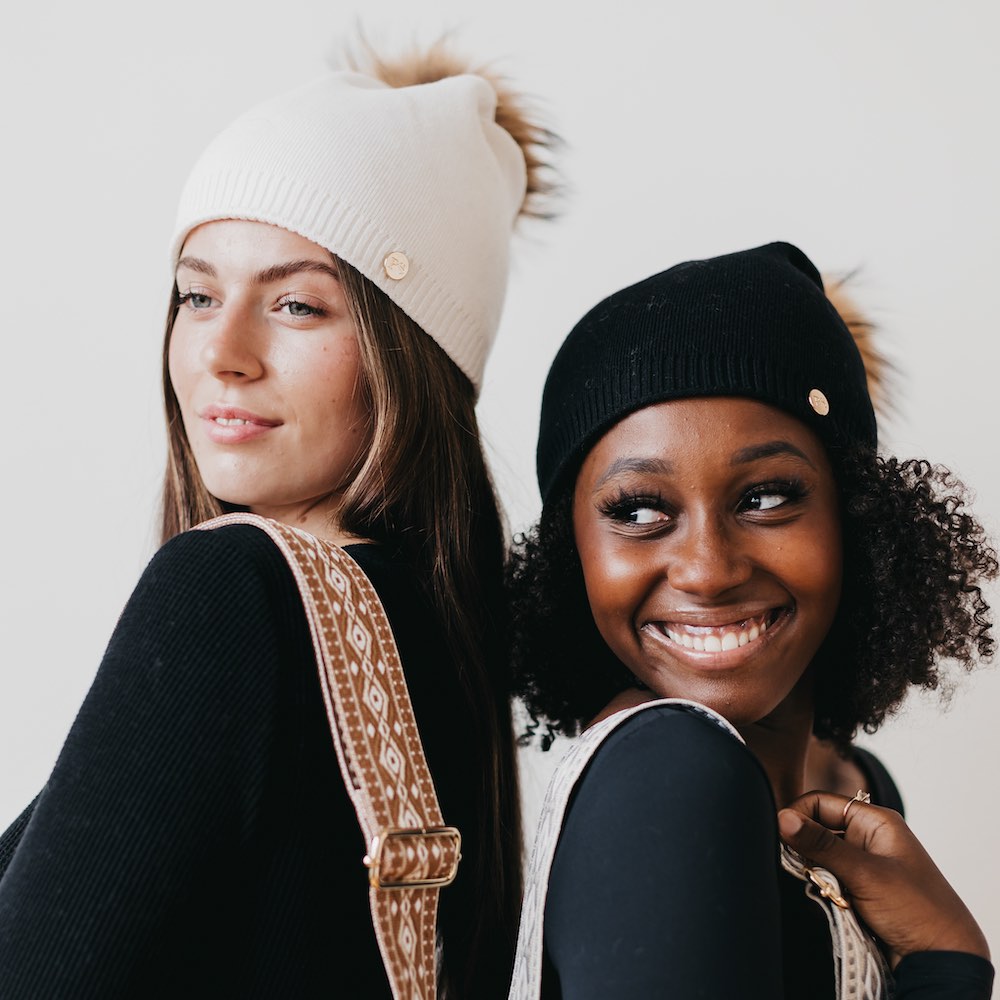 Cream and black knit slouchy beanies with ribbed cuffs, buttons, and fur poms