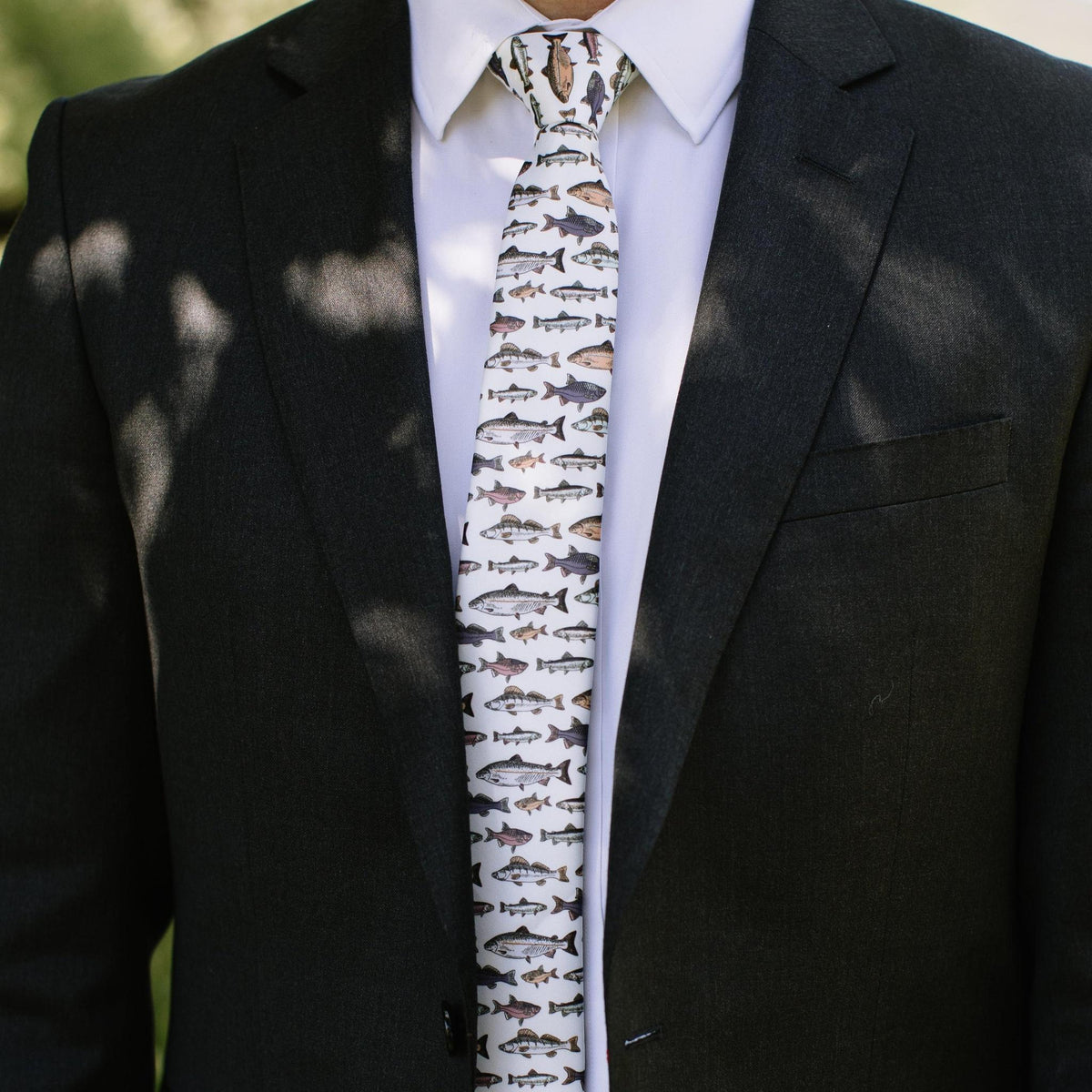 Men's fish-pattern necktie on black suit jacket, white base with small fish motifs