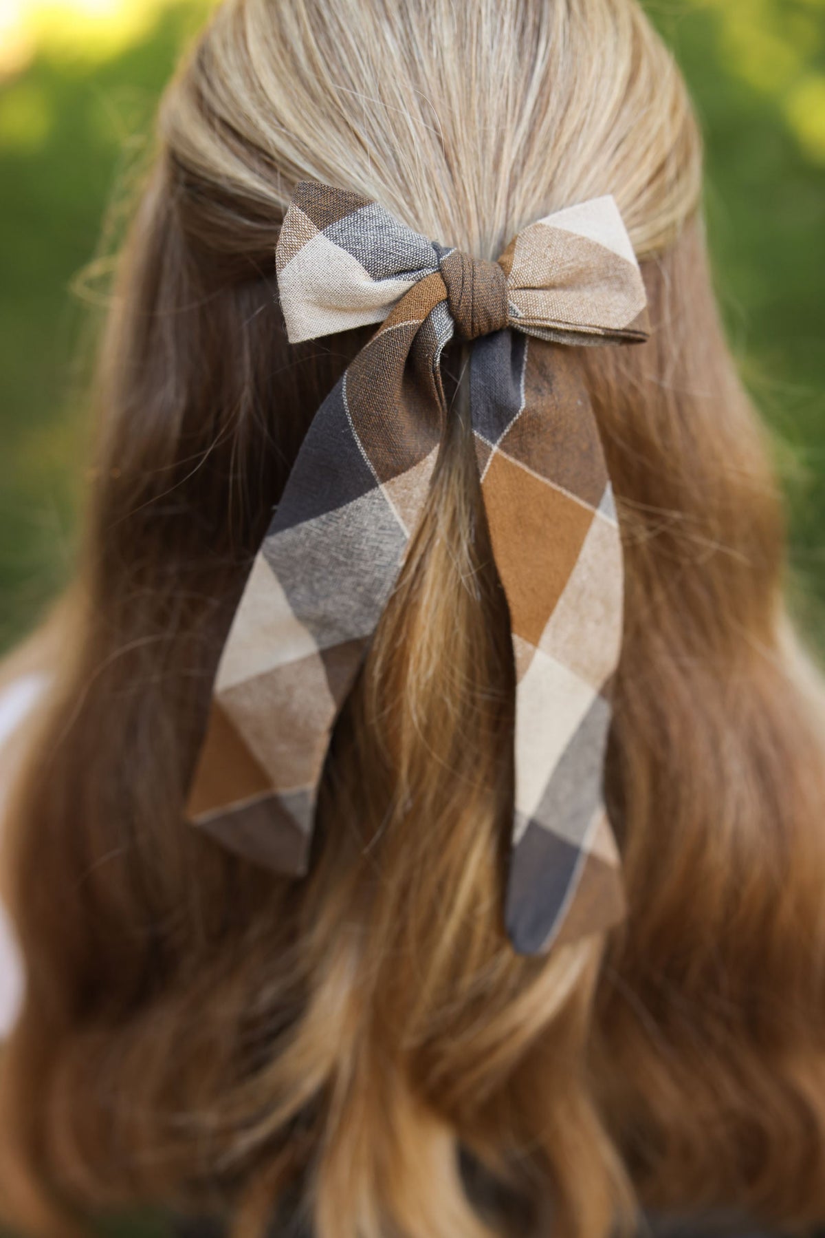 Plaid hair bow on model’s hair, tan, gray, and cream diamond pattern