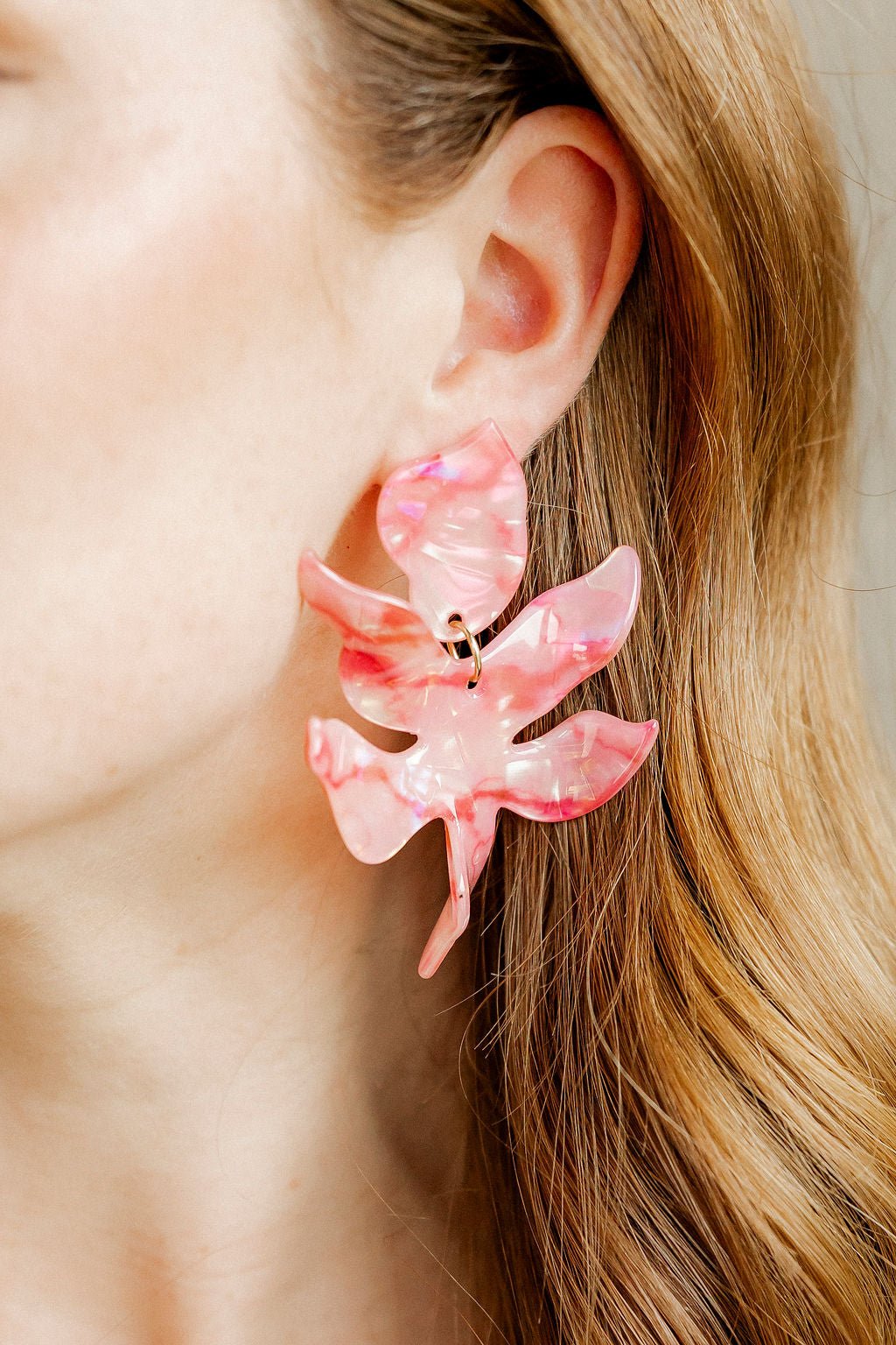 Close-up of pink translucent floral earrings with layered petals and gold hoop backs