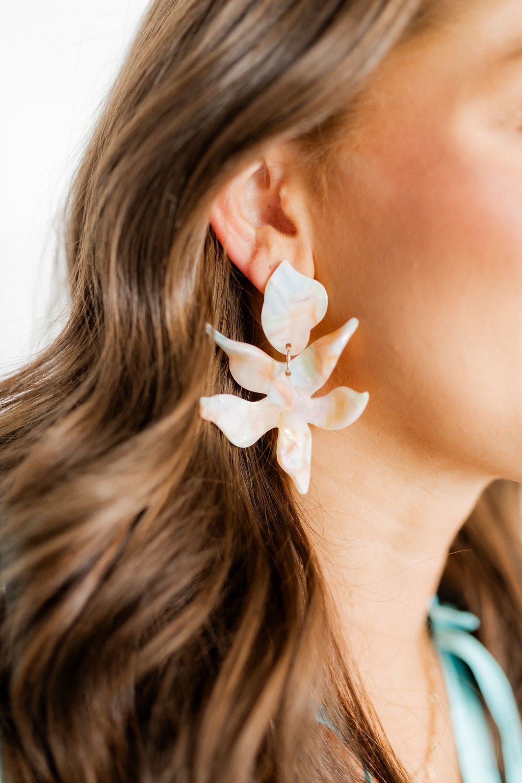 Iridescent white floral statement earrings with gold-tone accents, side profile