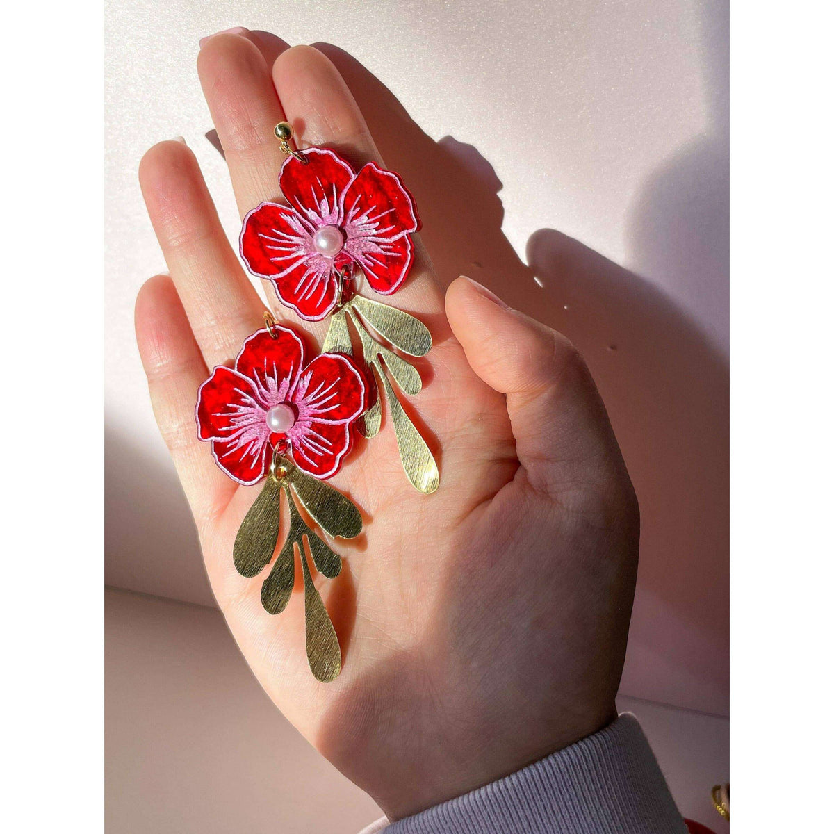 Pair of red acrylic blossom earrings with pearl centers and dangling gold leaves