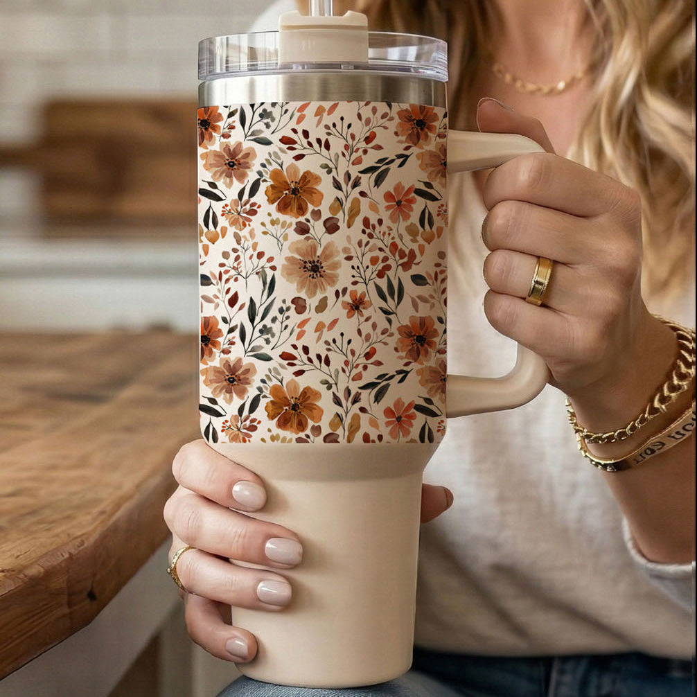 Floral travel tumbler with clear lid and straw, held by the handle