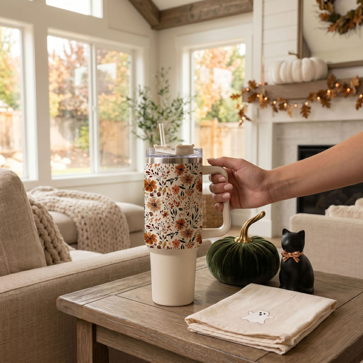 White travel tumbler with handle, straw, and autumn floral sleeve on table