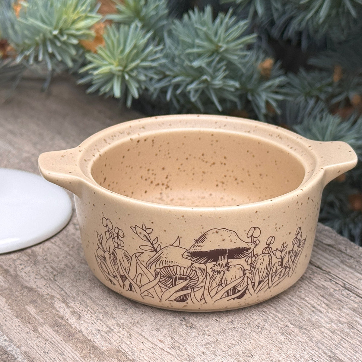 Beige ceramic trinket box with white lid resting nearby; forest engraving on body