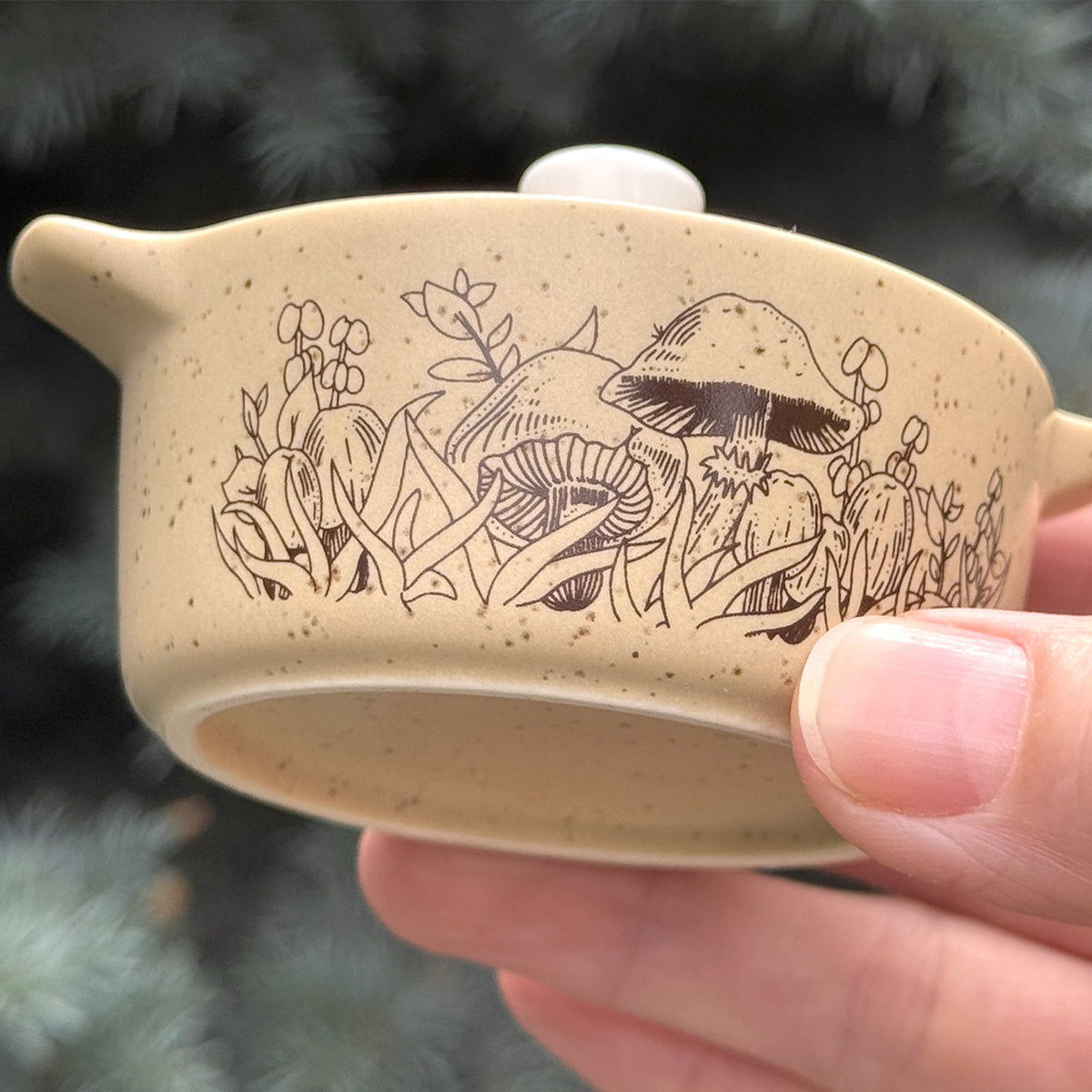 Close-up of beige ceramic trinket box lid edge and forest engraving with hand grip