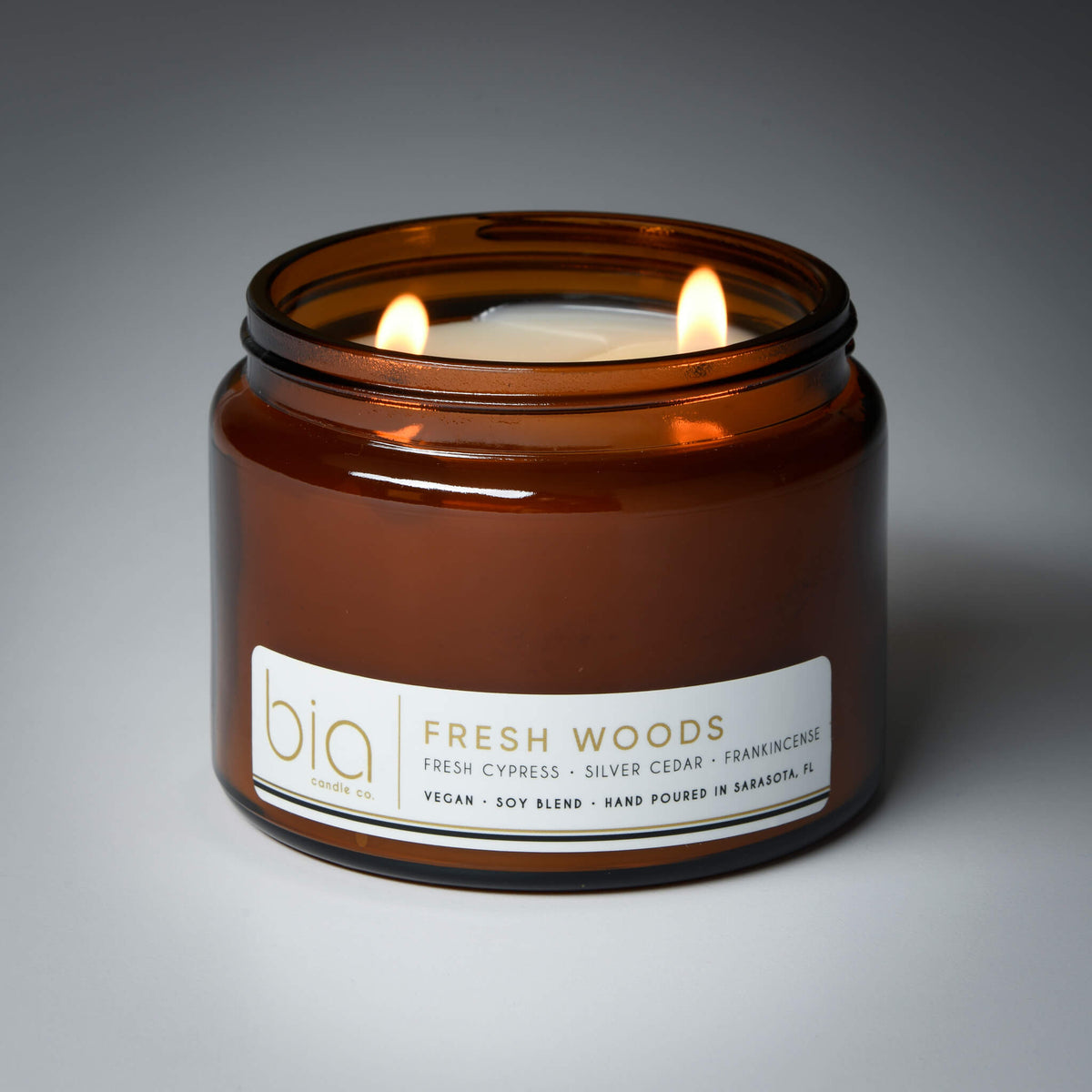 Lit Fresh Woods candle in a wide amber glass jar with a white label