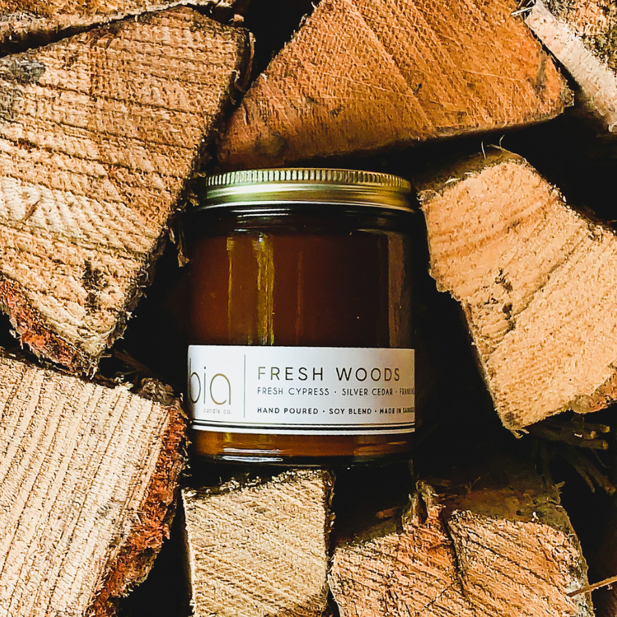 Fresh Woods candle in a lidded amber jar nestled among cut logs