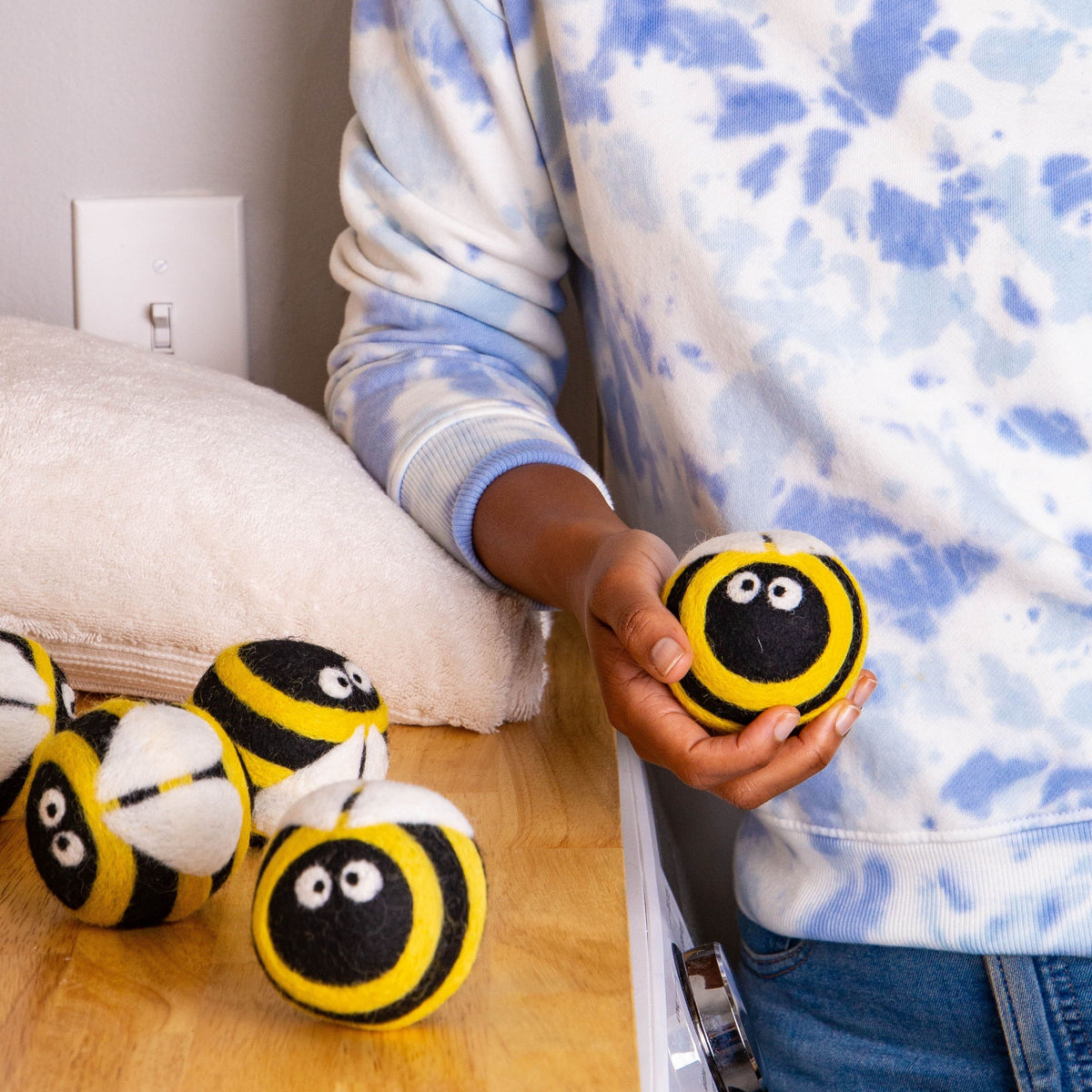 Plush bee dryer ball in hand, yellow-and-black striped plush with smiling white eyes