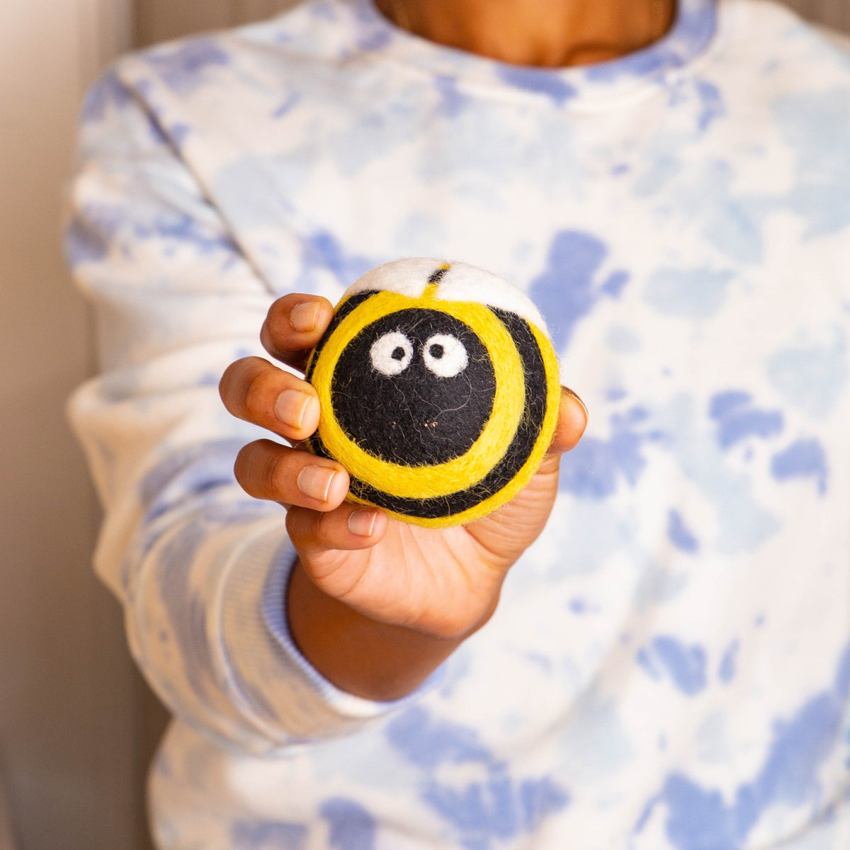 Plush bee dryer ball held in hand, yellow-and-black striped with friendly white eyes