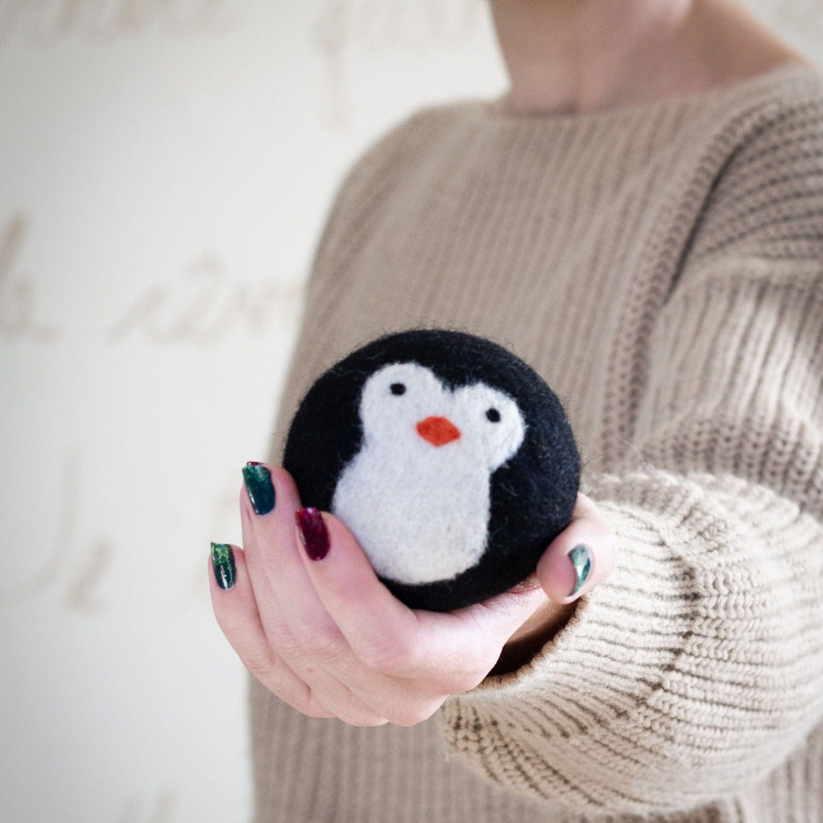 Penguin dryer ball held in a person’s hand with black-and-white plush face