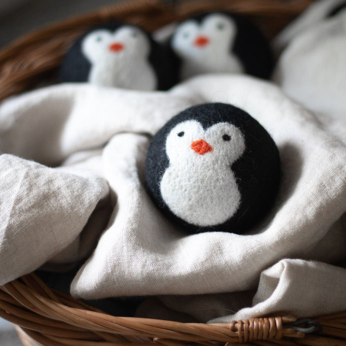 Penguin dryer ball resting on a cloth inside a wicker basket with other balls
