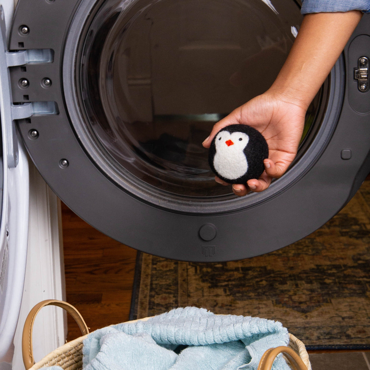 Black-and-white penguin plush toy held near a washing machine door