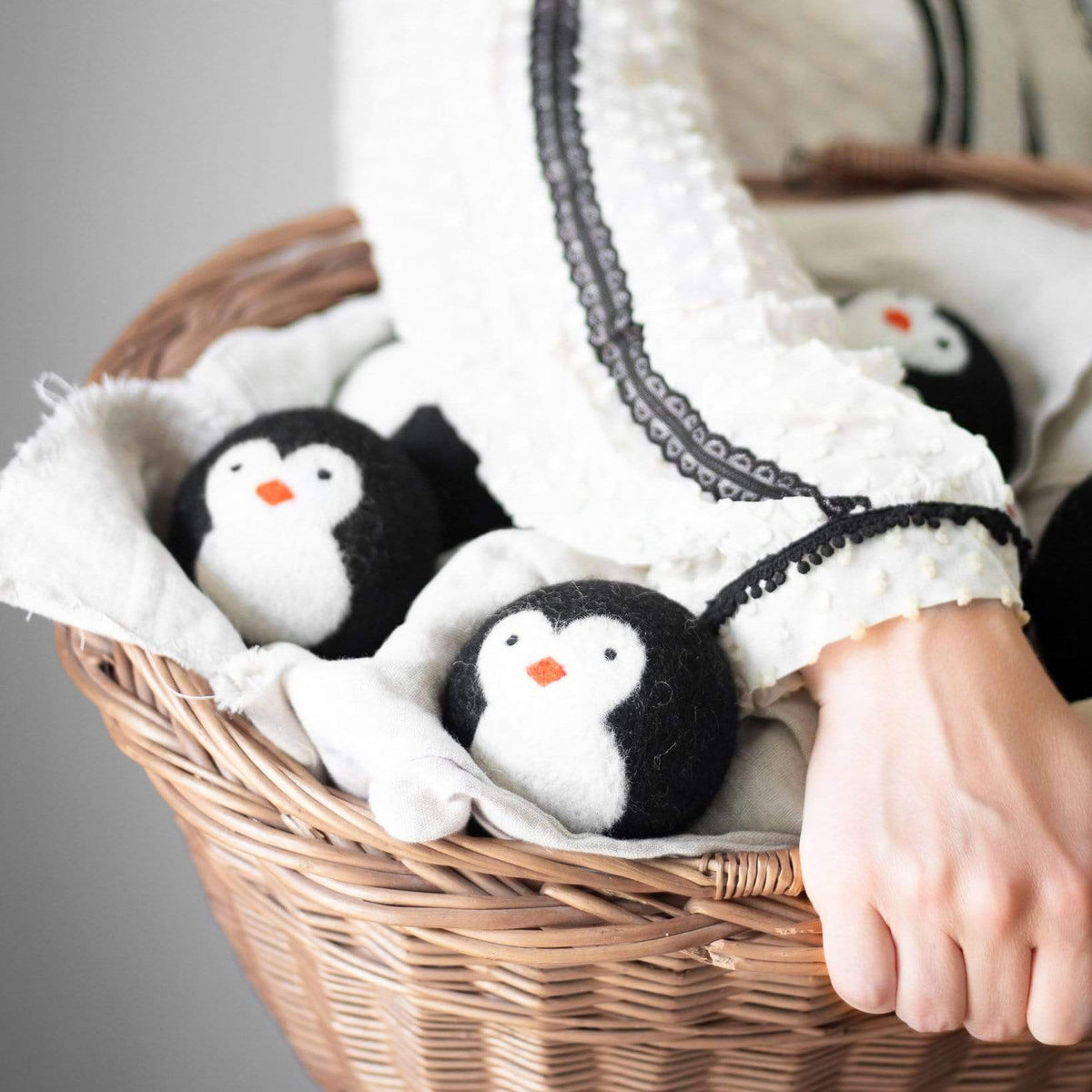 Close-up of penguin dryer balls in a wicker basket with a hand holding one ball
