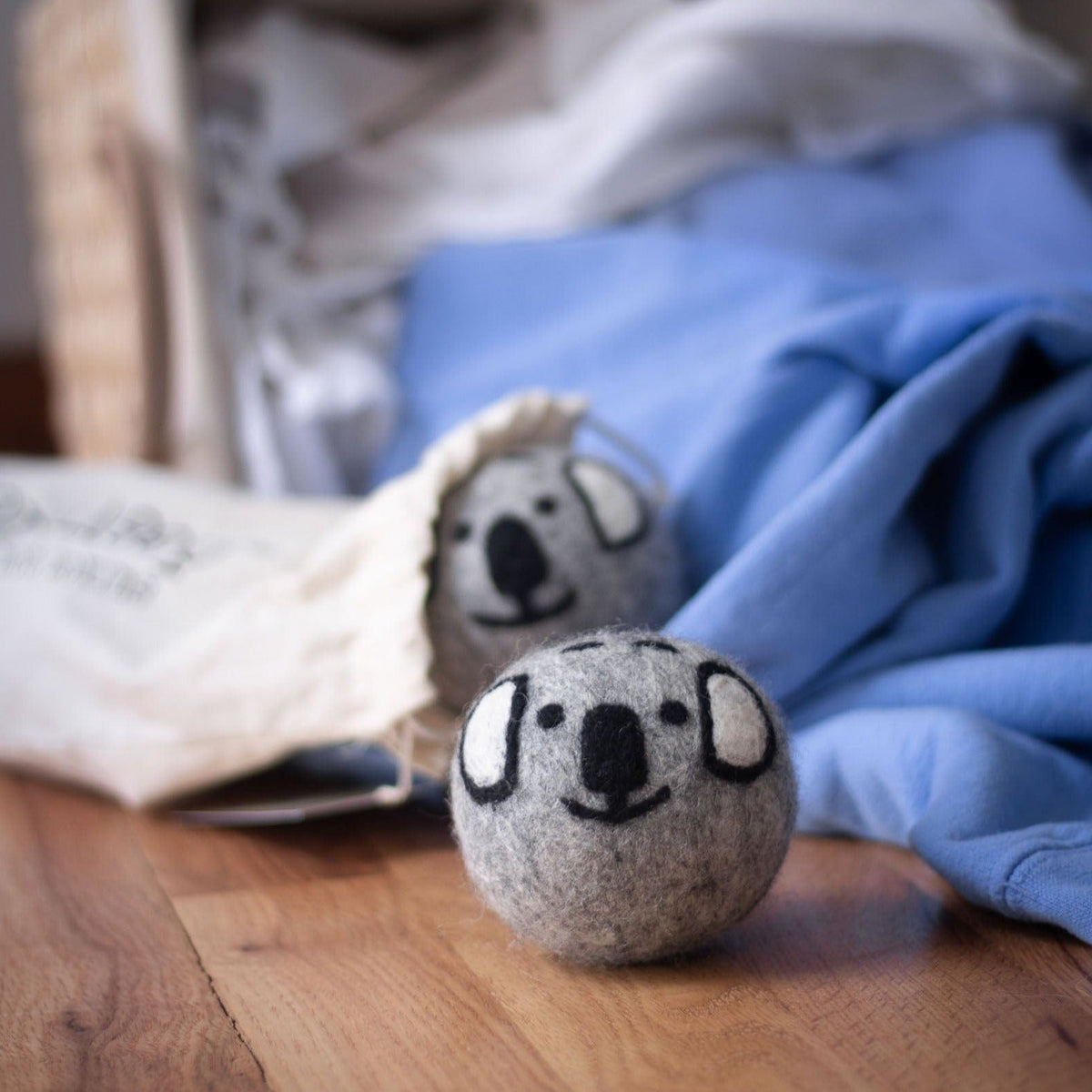 Single gray koala plush ball lying on a wooden surface beside folded blue cloth