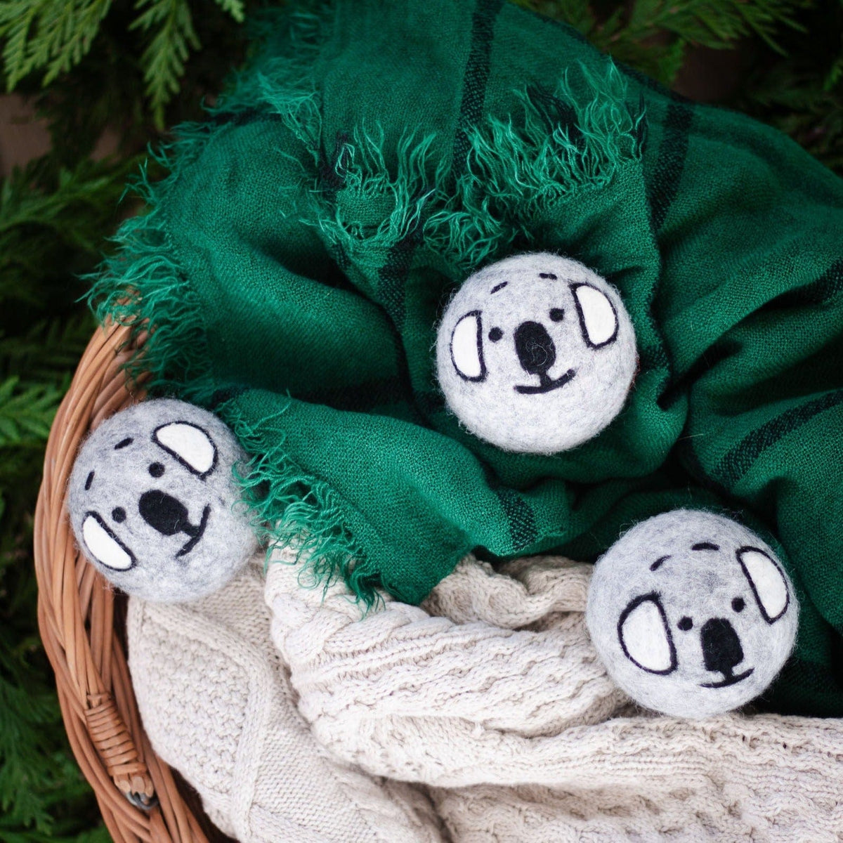 Gray koala plush balls tucked into green cloth and cream knit in a basket