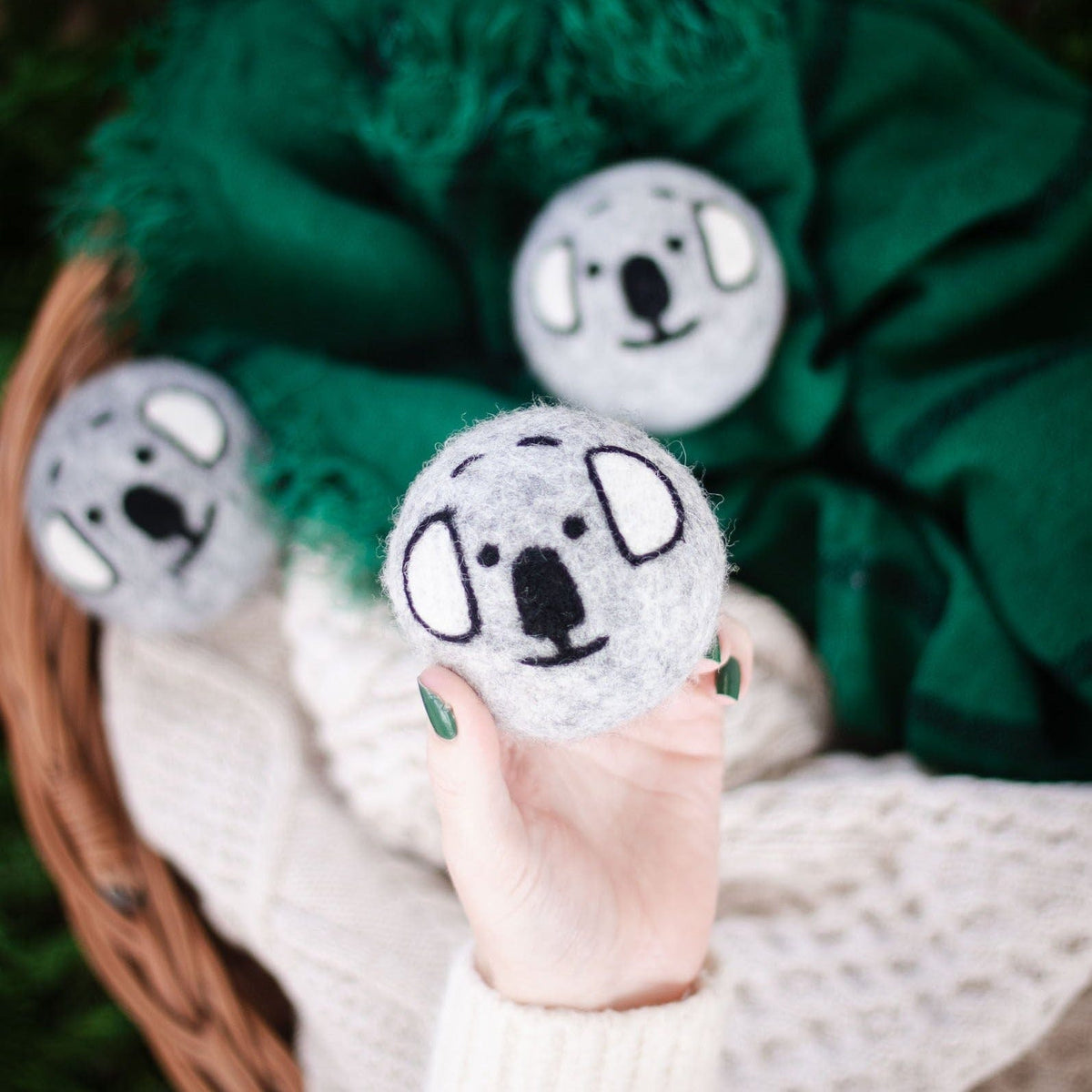 Three gray koala plush balls on green blanket in a wicker basket