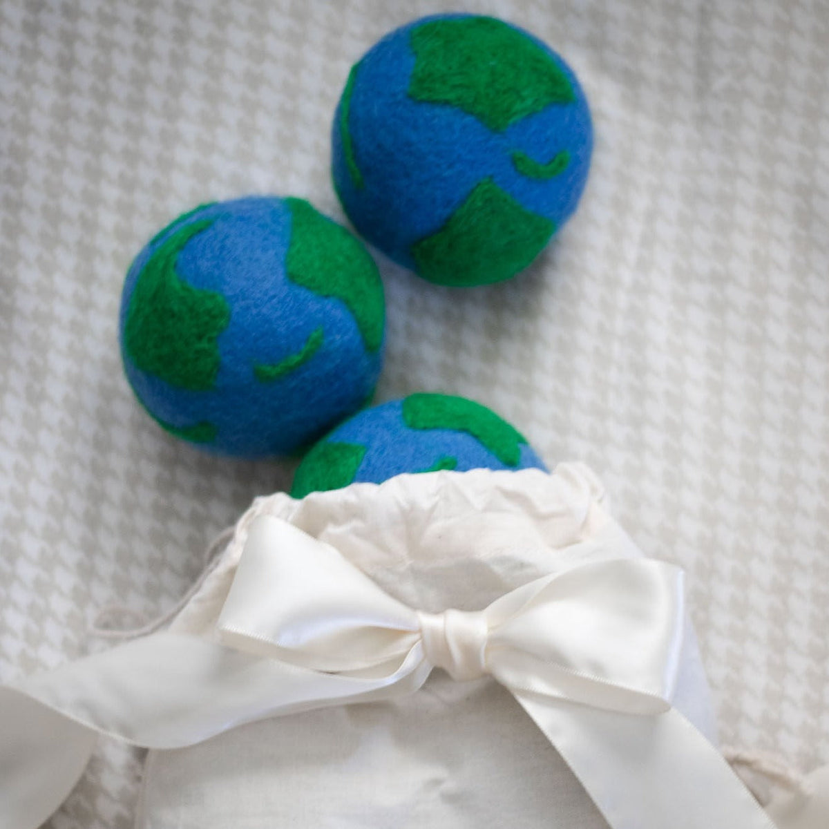 Three felt globe plush balls with blue and green patterns, tied with white bow