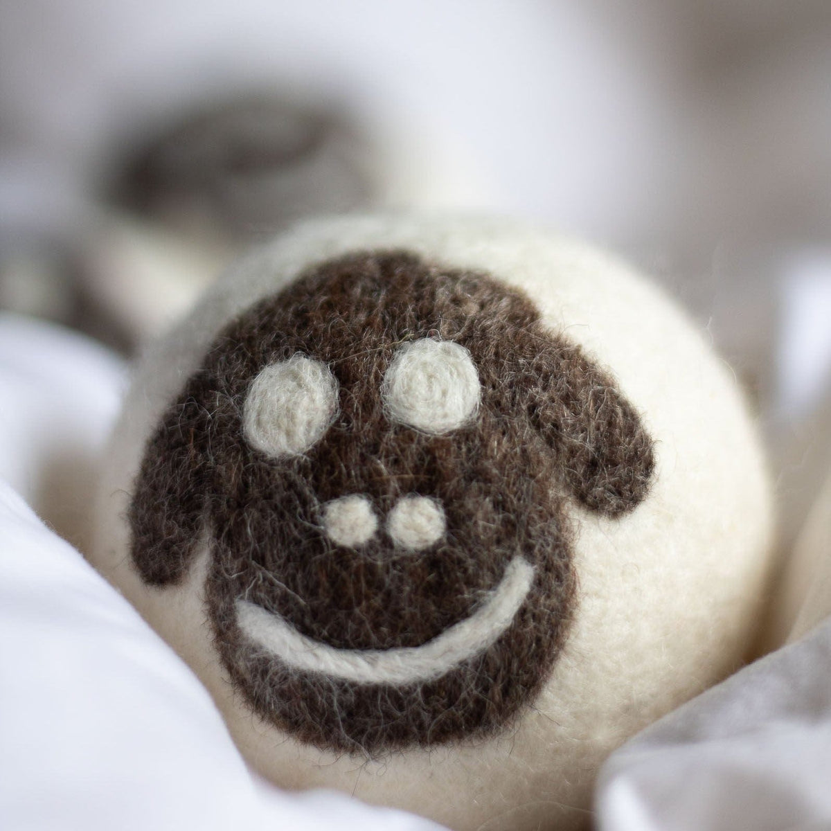 Single felt wool sheep dryer ball with smiling face and white felt paws
