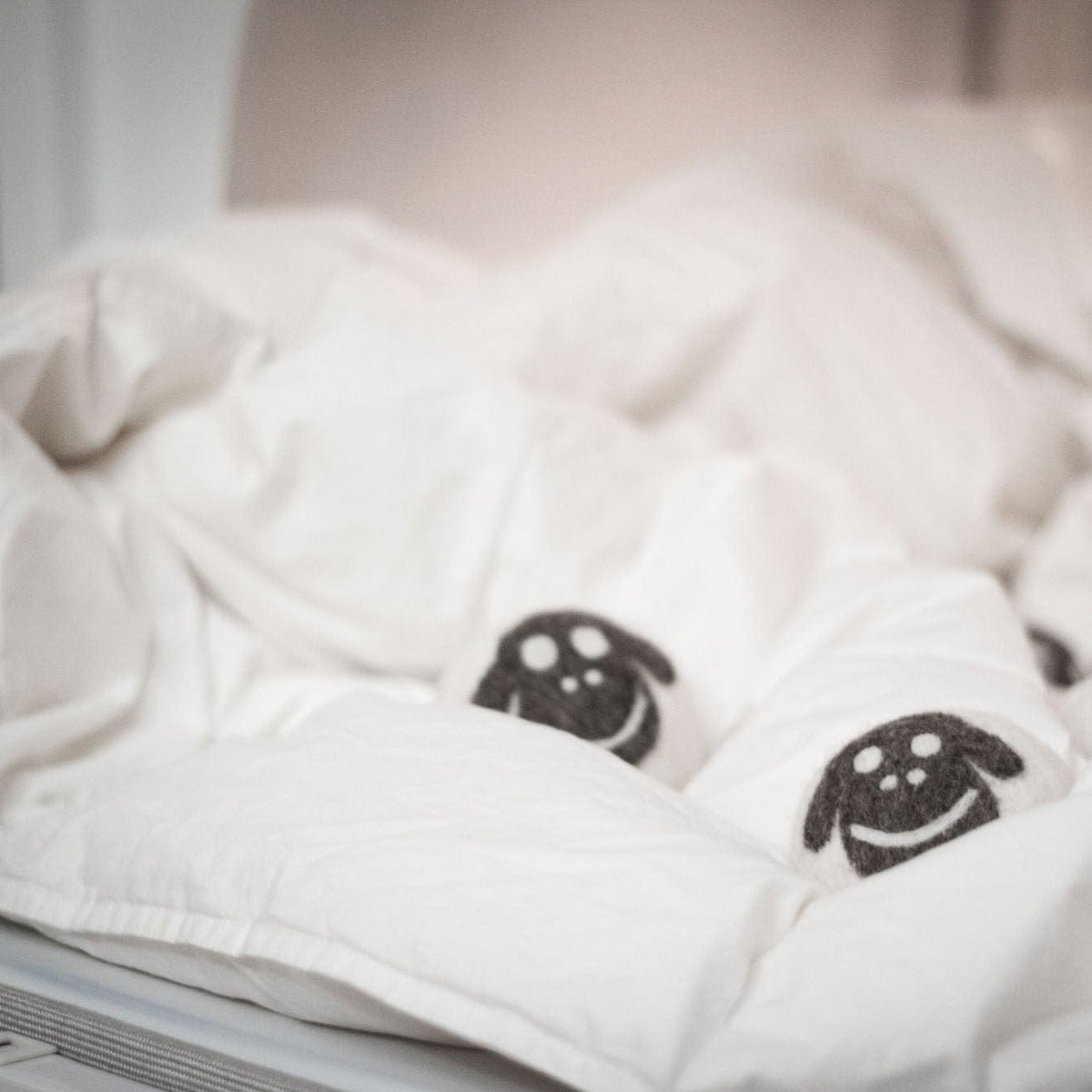 Wool sheep dryer balls on folded bedding, two smiling faces visible
