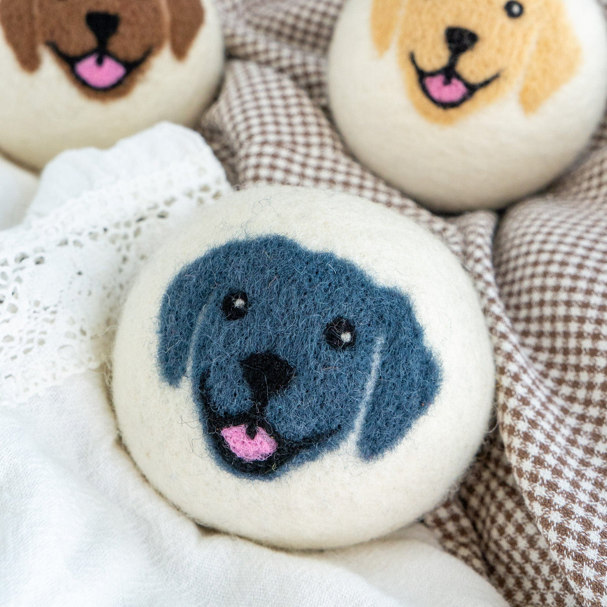 Blue felt dog-face button on white lace and plaid fabric, partial others visible.