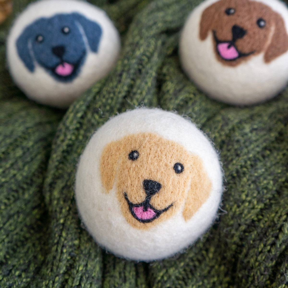 Felt dog-face button trio on green knit, one button in the foreground.