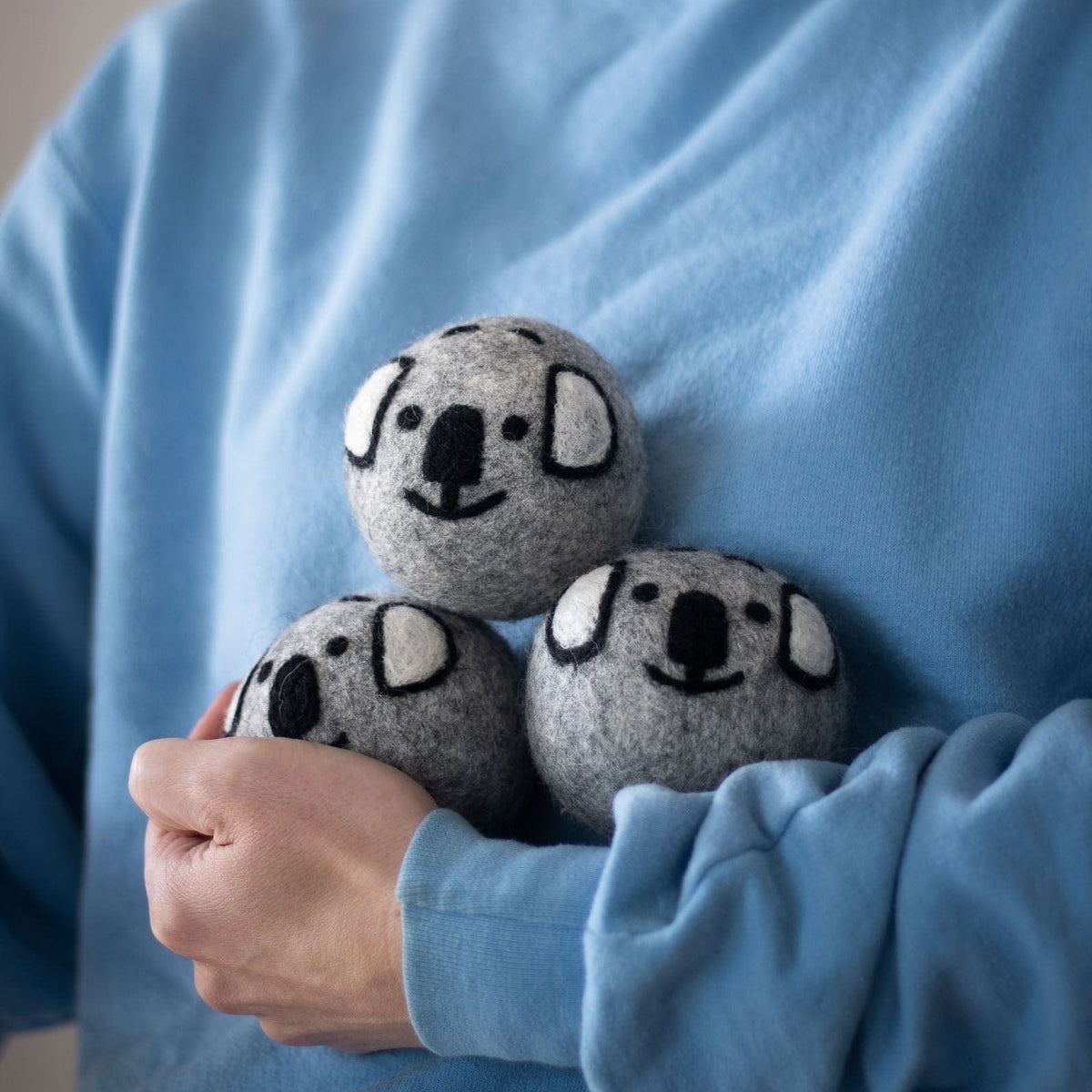 Gray koala dryer balls held in a person’s hands over a blue shirt