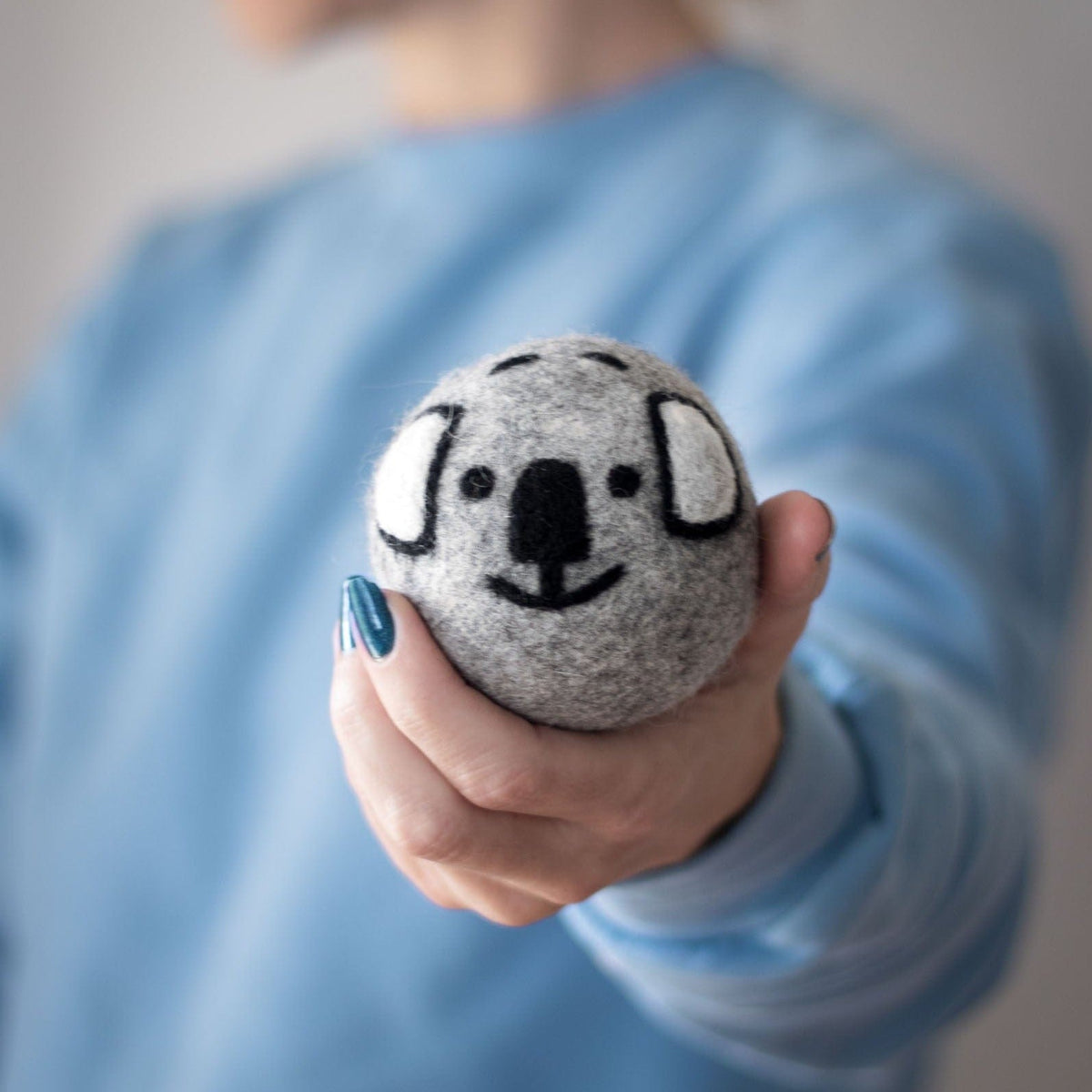 Person holding a gray koala dryer ball over a blue shirt