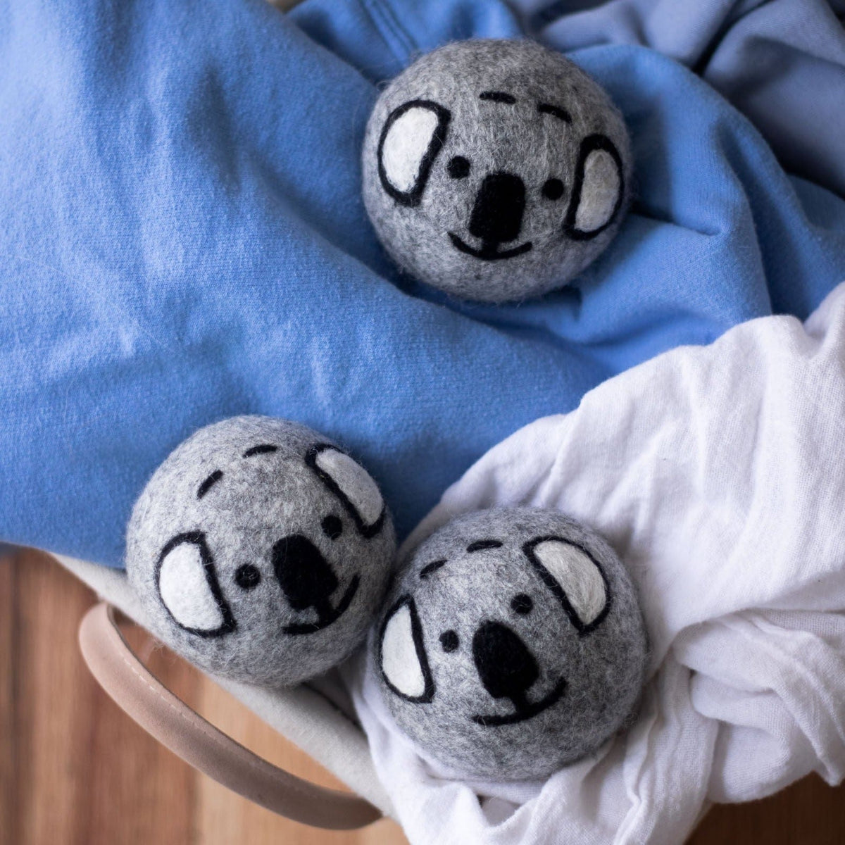 Three gray koala dryer balls tucked into a white and blue blanket