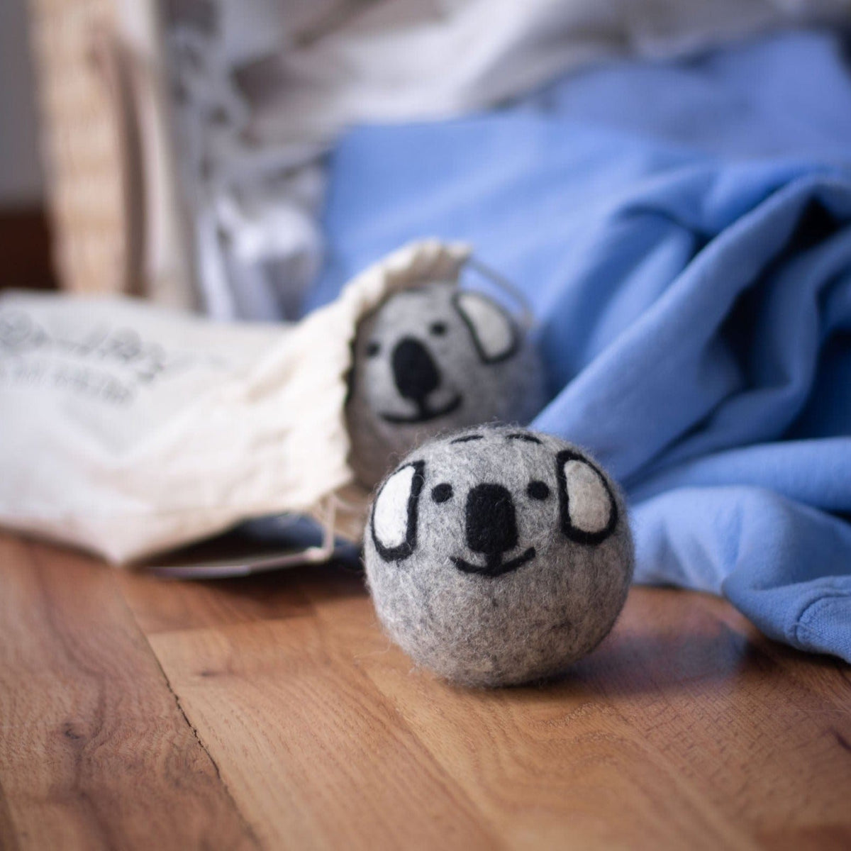 Gray koala dryer ball on a wood floor beside a folded blanket and white cloth