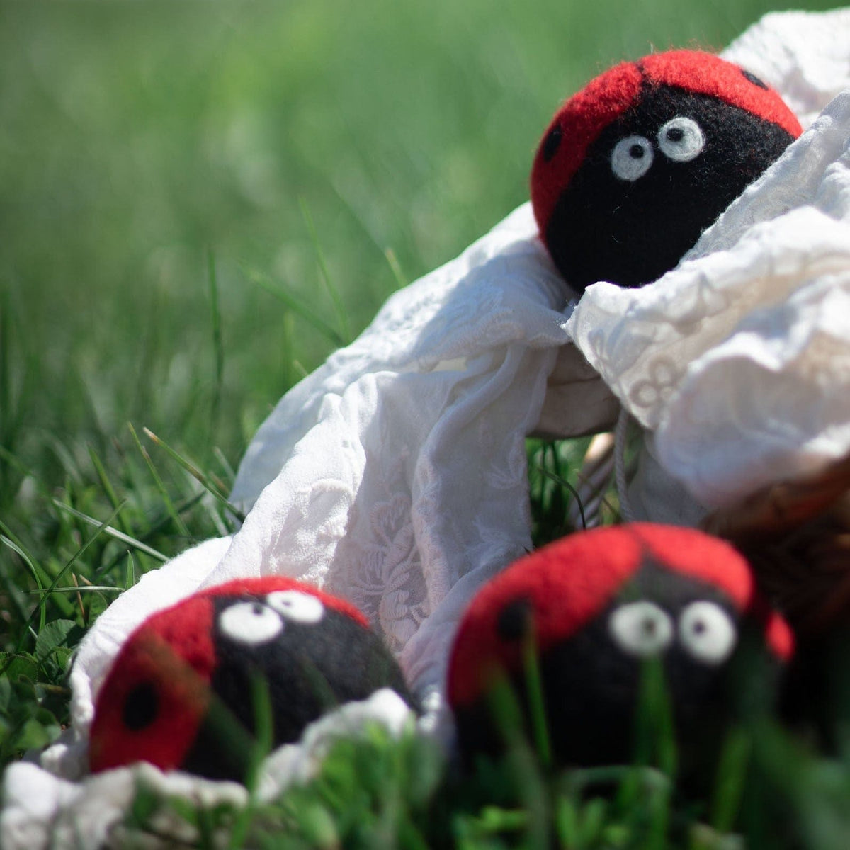 Plush ladybug trio partly tucked under white fabric, red wings and black bodies visible
