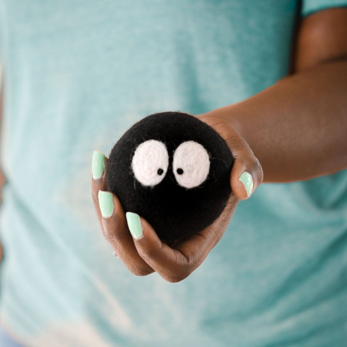 Hand holding a single black plush laundry ball with white felt eyes